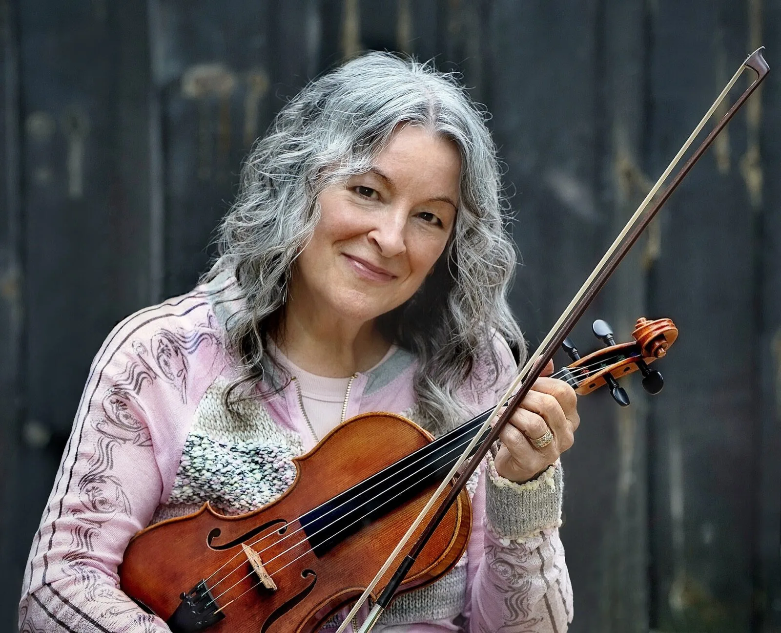 Cindy Thompson smiling and playing her fiddle outdoors.