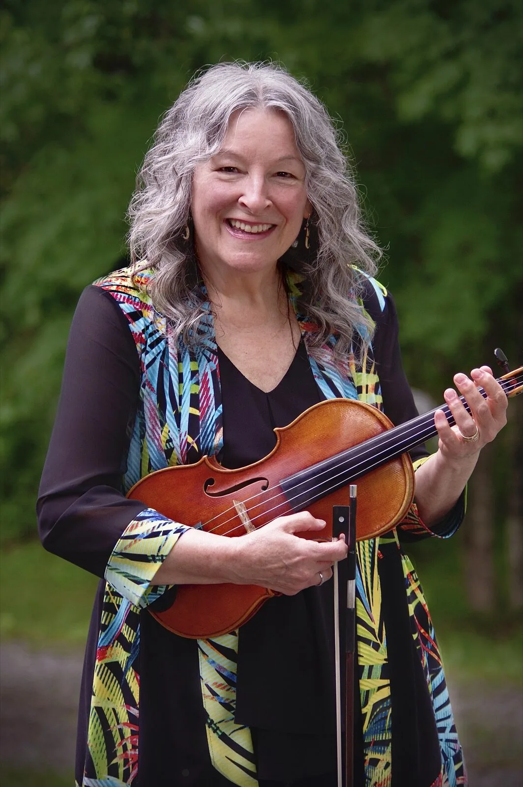 Cindy Thompson smiling and holding her fiddle outdoors.