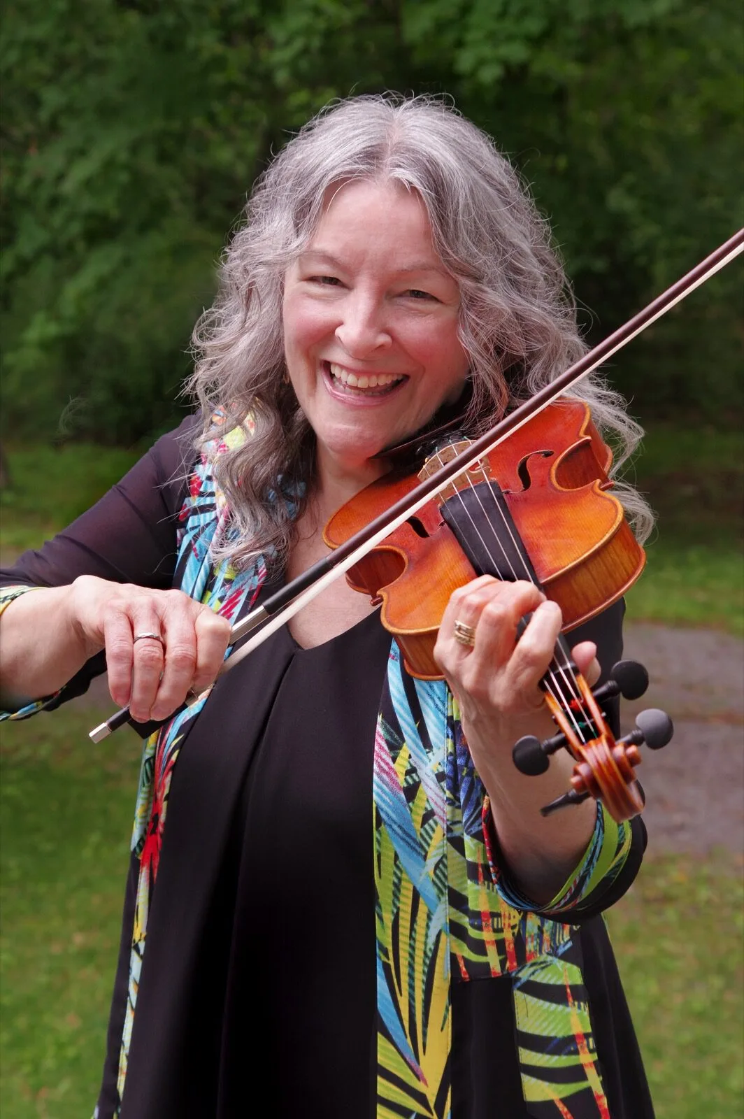 Cindy Thompson smiling and holding her fiddle outdoors.